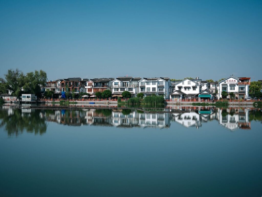 Charming traditional homes reflecting in calm lake waters under a clear blue sky.